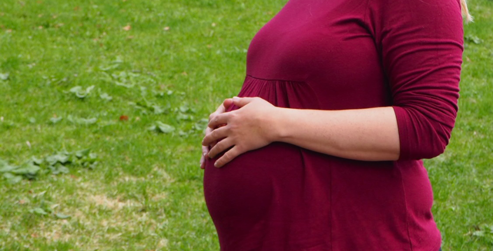 Gravid dame i r&oslash;d genser tar seg p&aring; magen. 