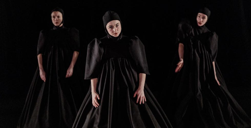 Tre dansere p&aring; en m&oslash;rk scene og sorte kostymer. 