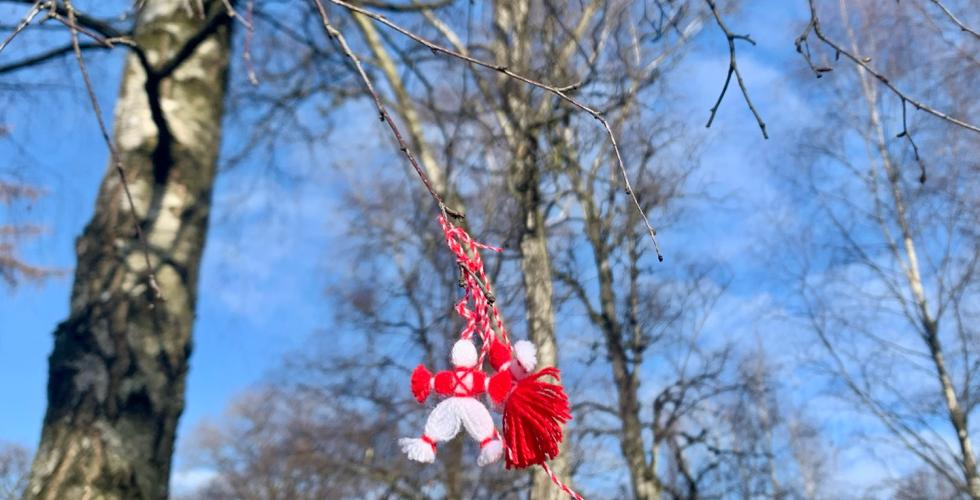 En r&oslash;d og hvit ulldekorasjon i form av to sm&aring; dukker henger i et tre.