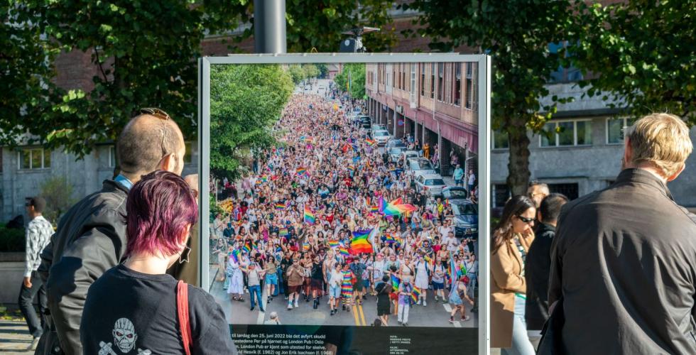 Folk st&aring;r og ser p&aring; et bilde av pride parade