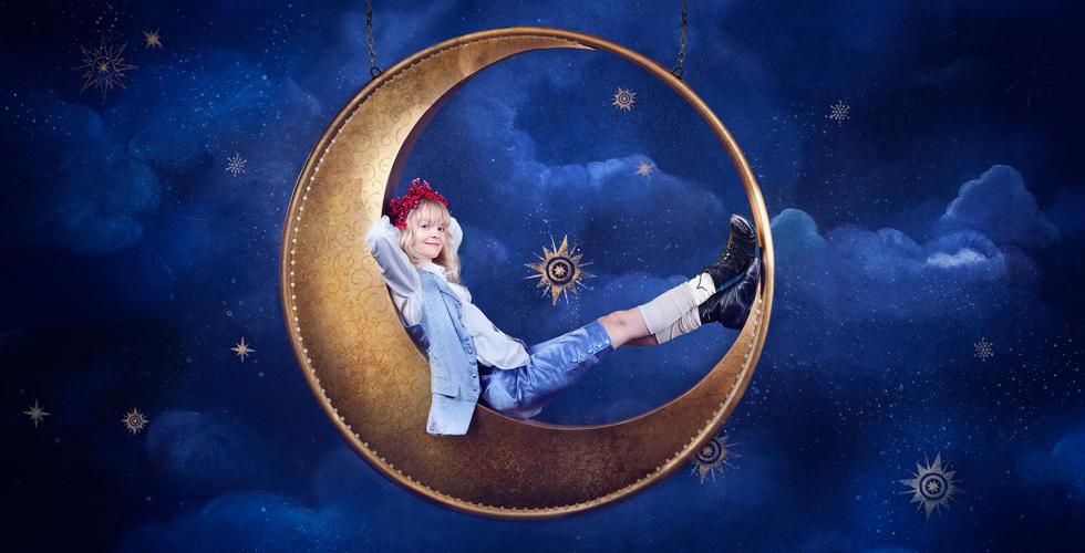 Monica Dybwad sitter i en halvm&aring;nerekvisitt med en bl&aring; bakgrunn.