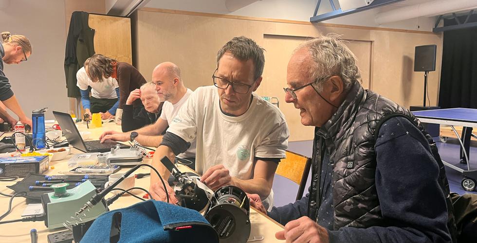 En eldre mann og en litt yngre mann sitter ved et bord og pr&oslash;ver &aring; fikse noe. 