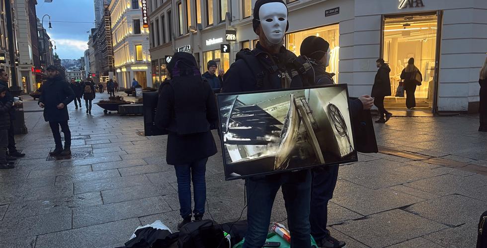 En mann med maske holder en tv-skjerm som viser videoer av dyr som blir mishandlet og slaktet p&aring; norske g&aring;rder 