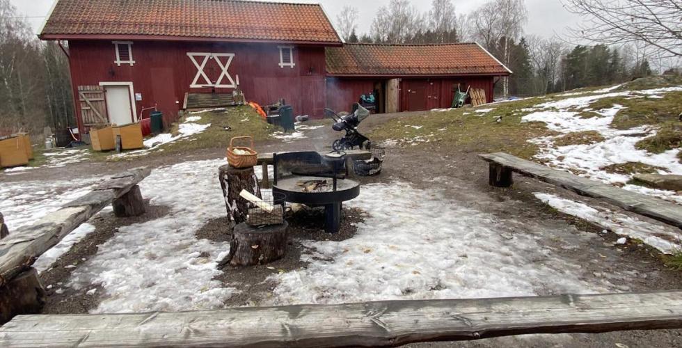 R&oslash;dt g&aring;rdsbruk om vinteren. Tre benker i front av bildet til &aring; sitte p&aring;, med et b&aring;l med r&oslash;yk i midten