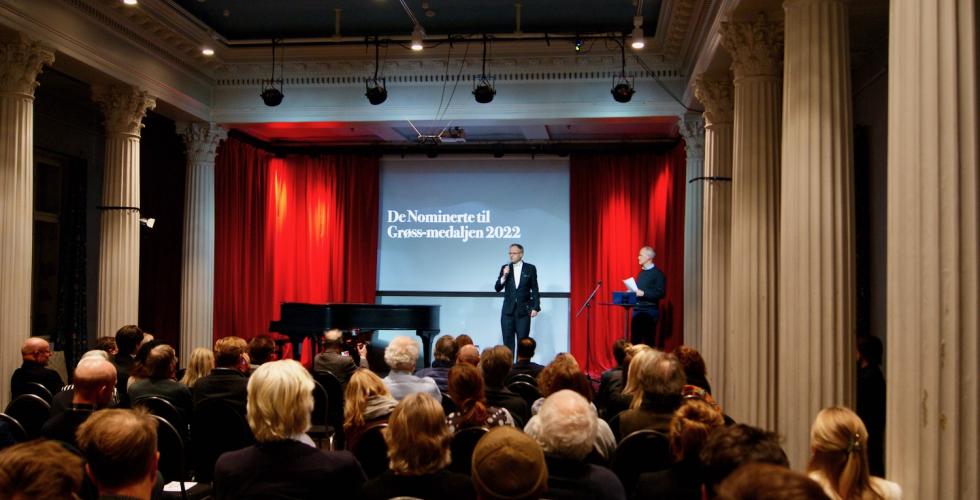 Mann st&aring;r p&aring; scene for &aring; presentere vinnere av gr&oslash;ssmedaljen