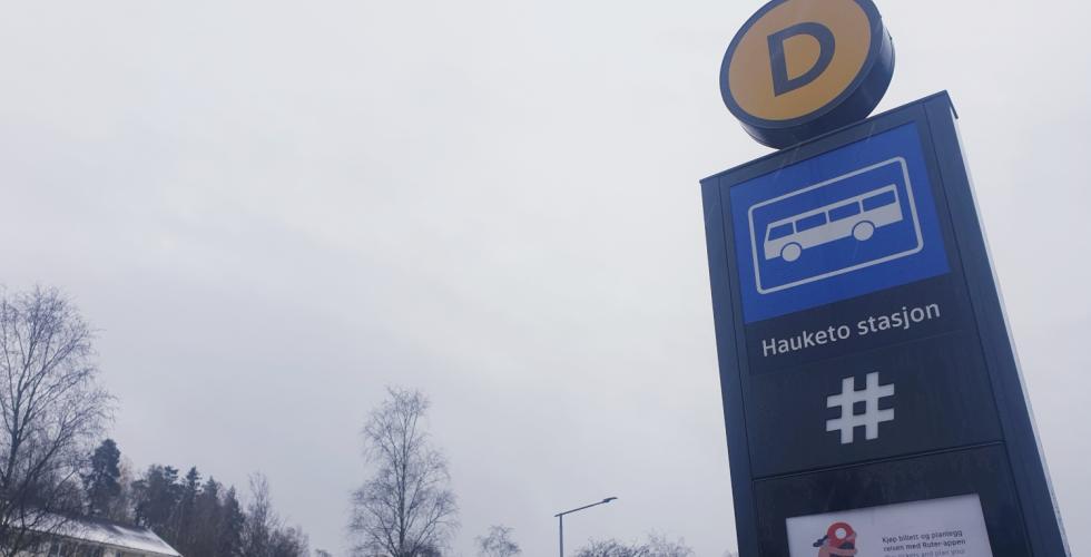 Gr&aring; himmel over et skilt for Hauketo bussholdeplass