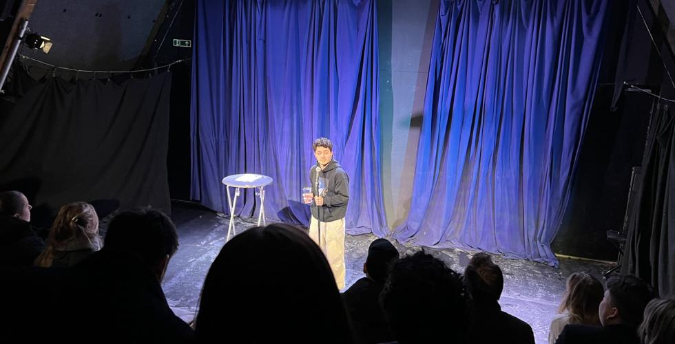 Komiker p&aring; scenen foran bl&aring; bakgrunn