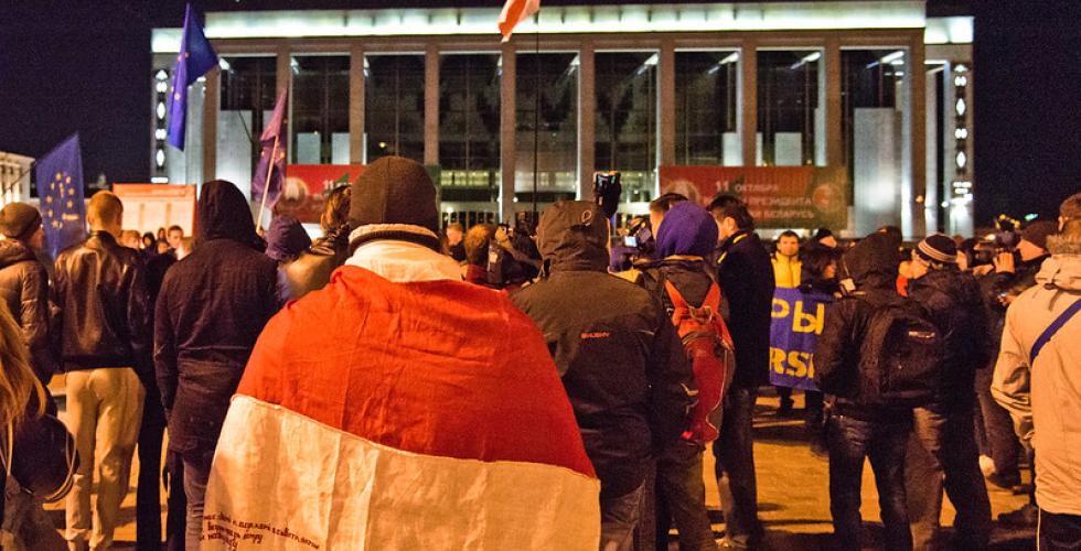 Et kveldsbilde, hvor hviterussiske demonstranter er samlet p&aring; et torg og b&aelig;rer det hvite og r&oslash;de flagget deres.