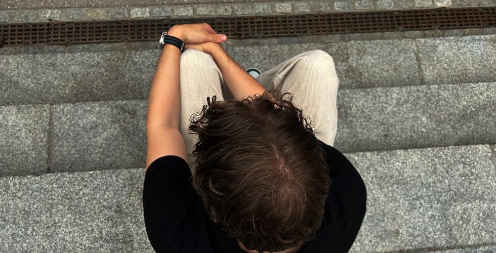 Gutt som sitter p&aring; trappen med hodet vendt ned, bildet er tatt ovenfra