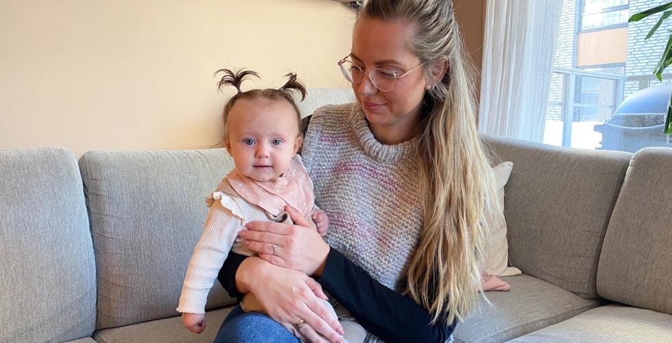 En kvinne sitter i sofaen med et barn p&aring; fanget. Barnet smiler