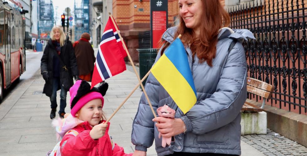 mor og datter p&aring; et fortau som holder det norske og det ukrainske flagget i kryss og smiler