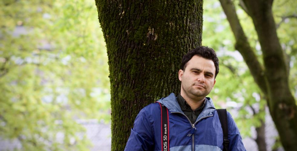 Javad Parsa med et kamera hengende over skulderen. Gr&oslash;nne tr&aelig;r i bakgrunnen.