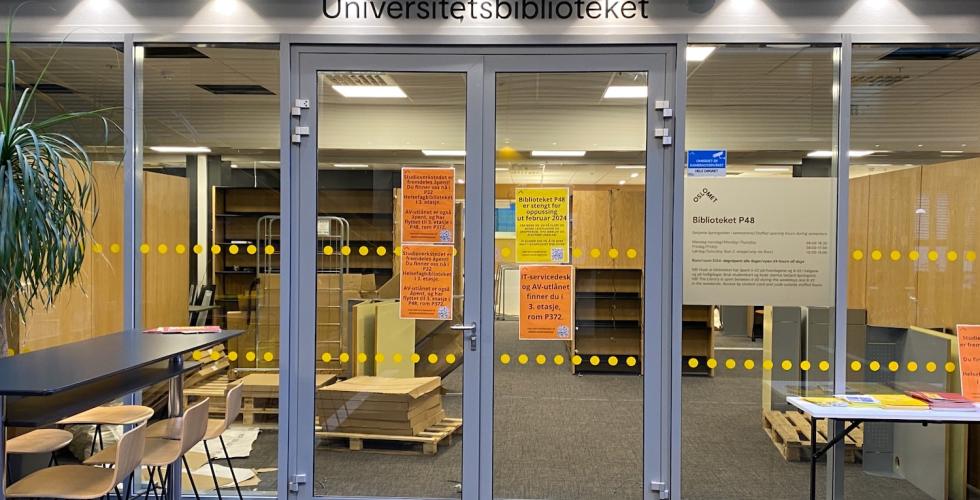Bildet viser utsiden av biblioteket p&aring; P48. Her ser man det henger flere plakater, som handler om at oppussingen kommer til &aring; vare ut februar, og hvor man kan finne hjelp. Igjennom vinduet kan man se at det fortsatt arbeides med montering.