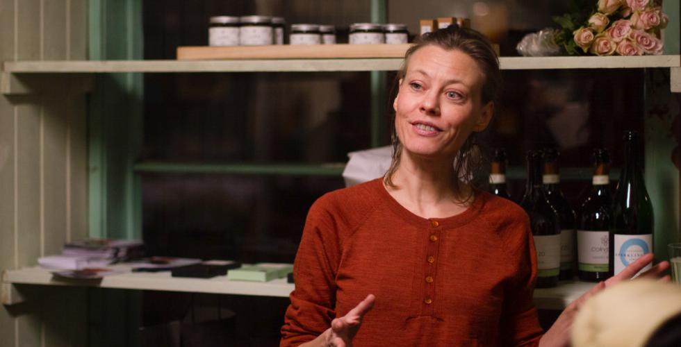 Fr&oslash;ydis Pedersen taler til menneskene som kom p&aring; &aring;pningen til hennes nye lokale p&aring; Salgshallen. Hun er ikledd en r&oslash;d topp fra eget inventar og bruker hendene mens hun snakker.