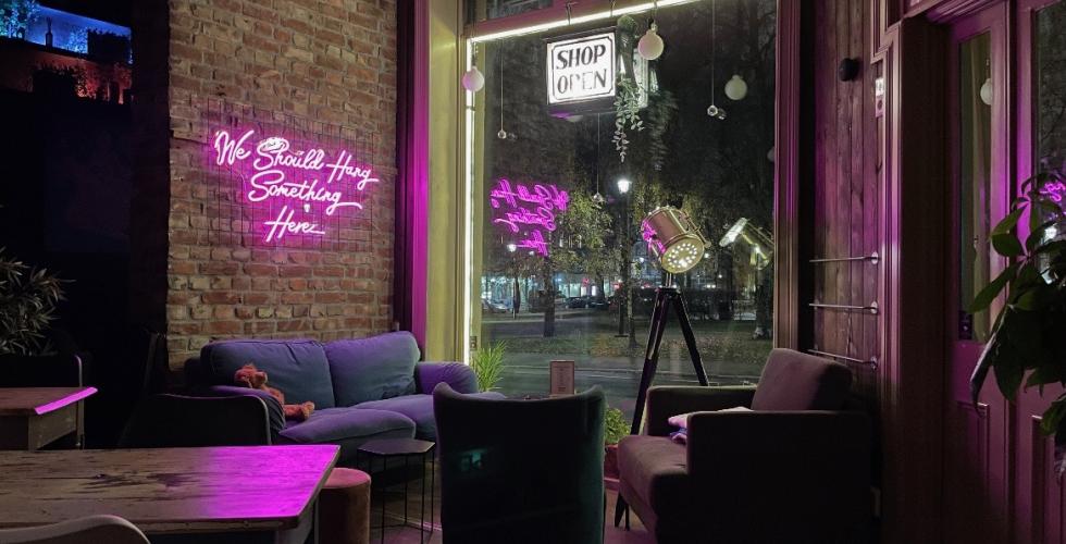 Bilde av lokale: et stort vindu i bakgrunn med en sofa og to stoler foran. Et neonrosa skilt p&aring; veggen