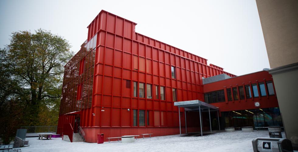 Sofienberg skole fotografert i under en gr&aring; himmel. Bygget er farget i en sterk r&oslash;dfarge. Skoleg&aring;rden er &aring; se i forgrunnen av bildet.