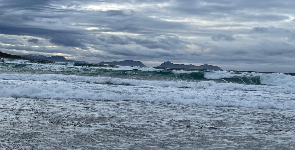 Hav med mange b&oslash;lger, og fjell i bakgrunnen
