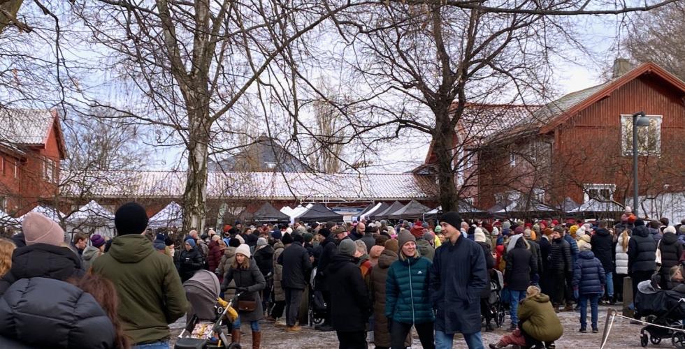 Bildet viser julemarkedet i Botanisk Hage. Det er mange folk som vandrer rundt, og vi kan se taket p&aring; bodene bak dem.