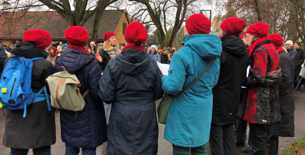 Koret har r&oslash;de luer og synger foran publikum