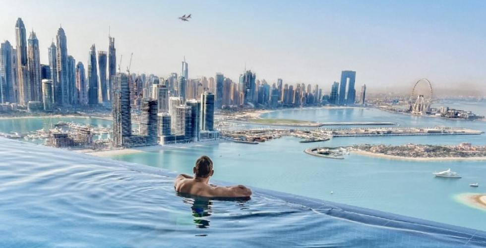 Skallet mann ser ut over Dubai fra et sv&oslash;mmebasseng