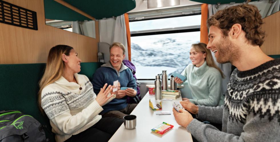 Glade passasjerer rundt bord p&aring; toget.