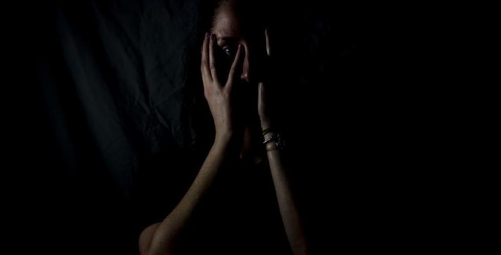 Kvinne ser skremt ut og gjemmer seg i m&oslash;rket.