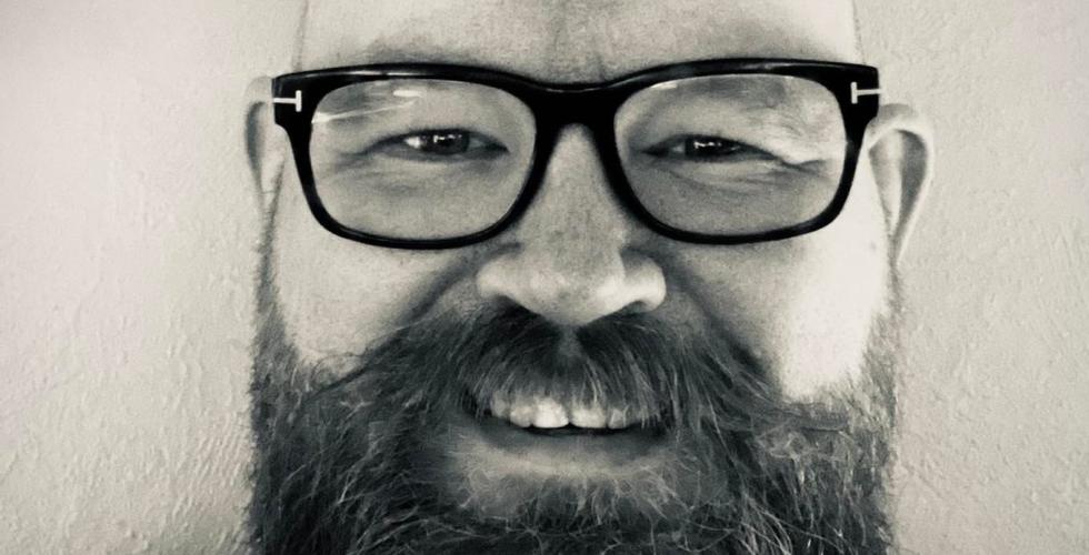 Gr&aring;tt og hvitt portrettbilde av Lars Martin Torp. Med stort smil, skallet hode, svarte briller og stort skjegg