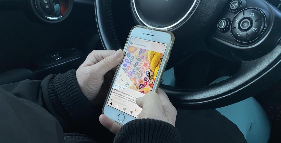 En kvinne har oppe Instagram p&aring; telefonen imens hun sitter bak rattet