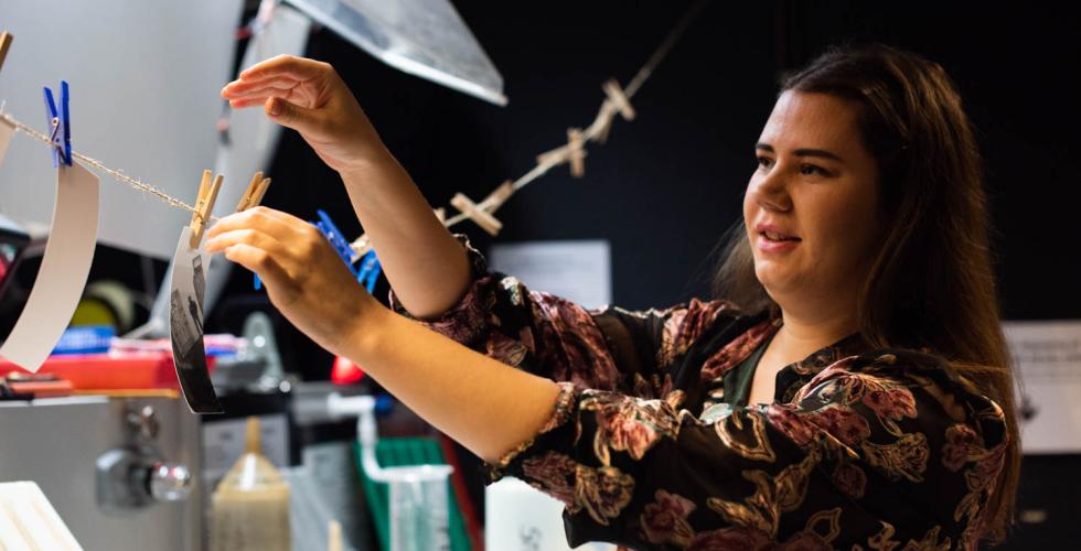 Hanne henger opp bilder p&aring; m&oslash;rkerommet.