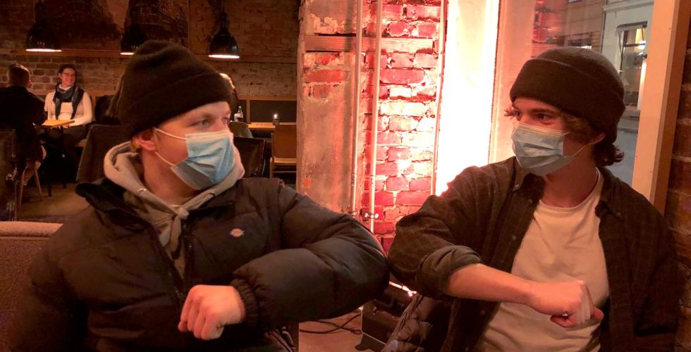 To gutter har p&aring; munnbind og dytter albuene mot hverandre