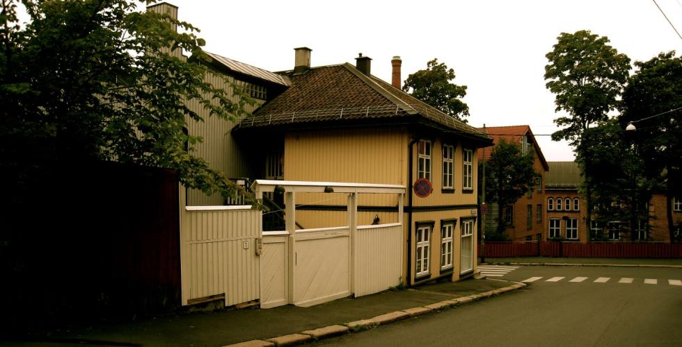 Bildet viser et gult hus, med et hvitt gjerde p&aring; siden. 