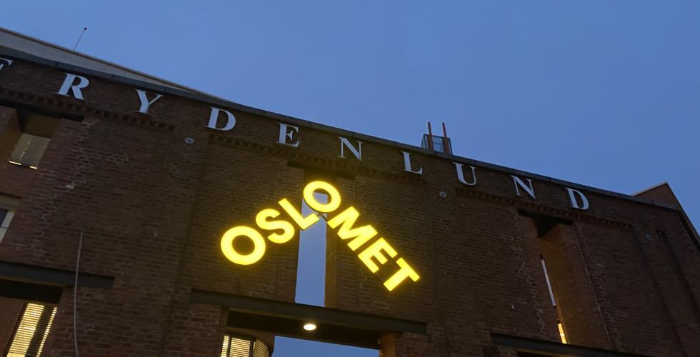 Det lysende gule OsloMet-skiltet p&aring; Frydenlund i m&oslash;rket.