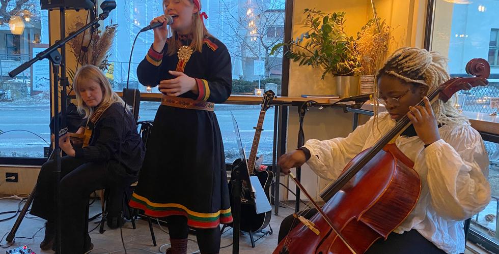 En samisk jente st&aring;r og synger inn i en mikrofon med band rundt seg