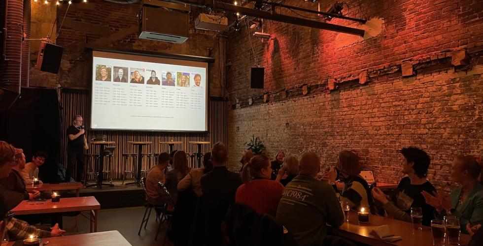 En stor scene hvor programlederes st&aring;r med en skjerm bak seg. Publikum ser opp mot skjermen og klapper. 