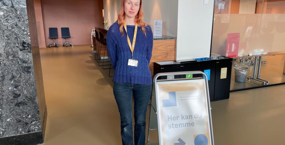 Valgmedarbeider Sunniva Harstein st&aring;r bak en plakat med teksten "Her kan du stemme".