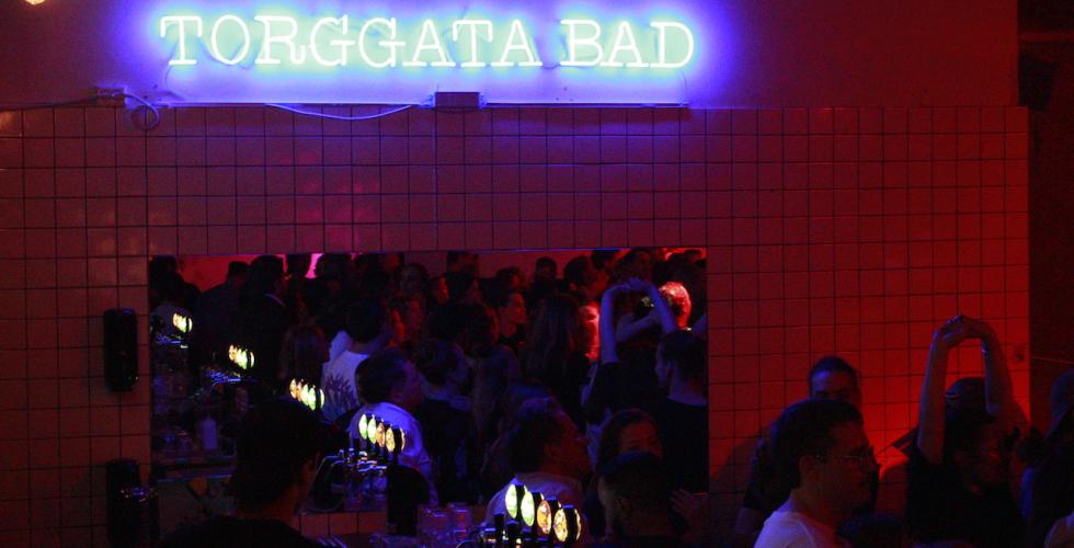 Et bl&aring;tt lys lyser opp et m&oslash;rkt danselokale. Man ser folk danse i speilbildet. 