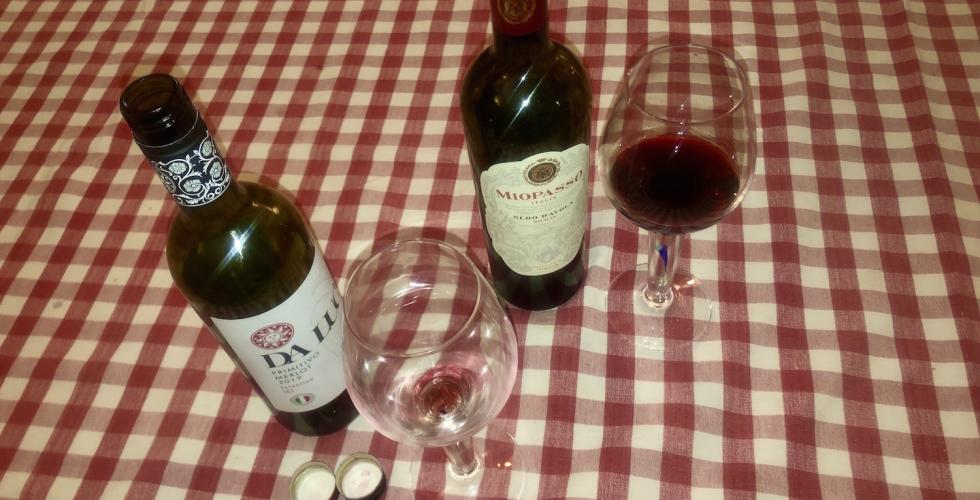 To flasker, og et glass som st&aring;r p&aring; et bord med r&oslash;dt og hvit rutete duk