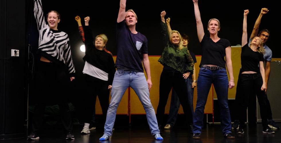 NI personer st&aring;r med en h&aring;nd i v&aelig;ret oppe p&aring; en scene