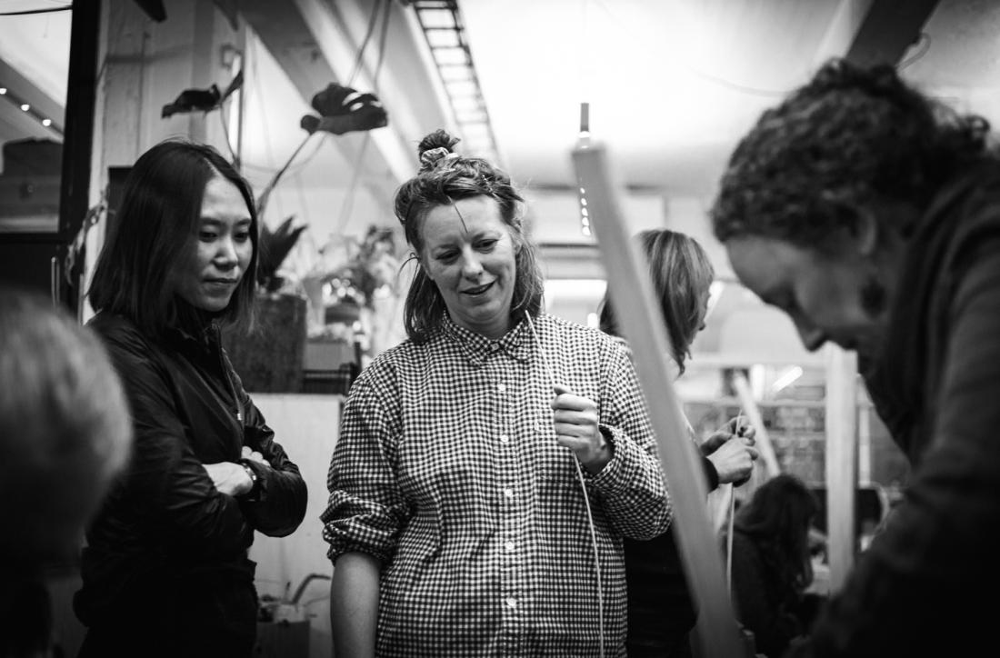 Tre kvinner st&aring;r rundt leder for &aring; l&aelig;re kurvfletting 