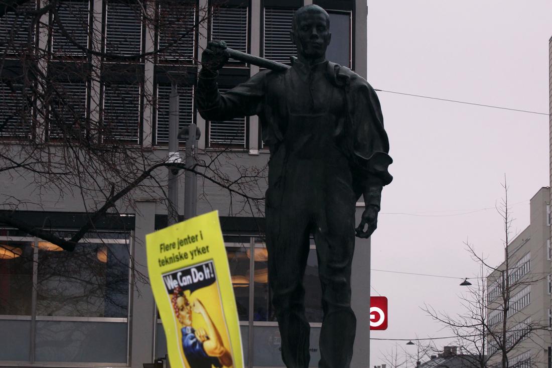 plakat der det står "Flere jenter i tekniske yrker, sats på jenter i yrkesfag" med et bilde av Rosie the Riveter og "we can do it"-slagordet hennes foran statuen av LO-mannen