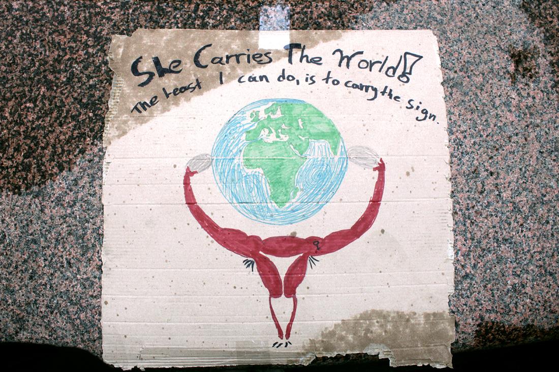 Plakat der det står She carries the world - the best I can do is to carry the sign, med bilde av en livmor som bærer verden